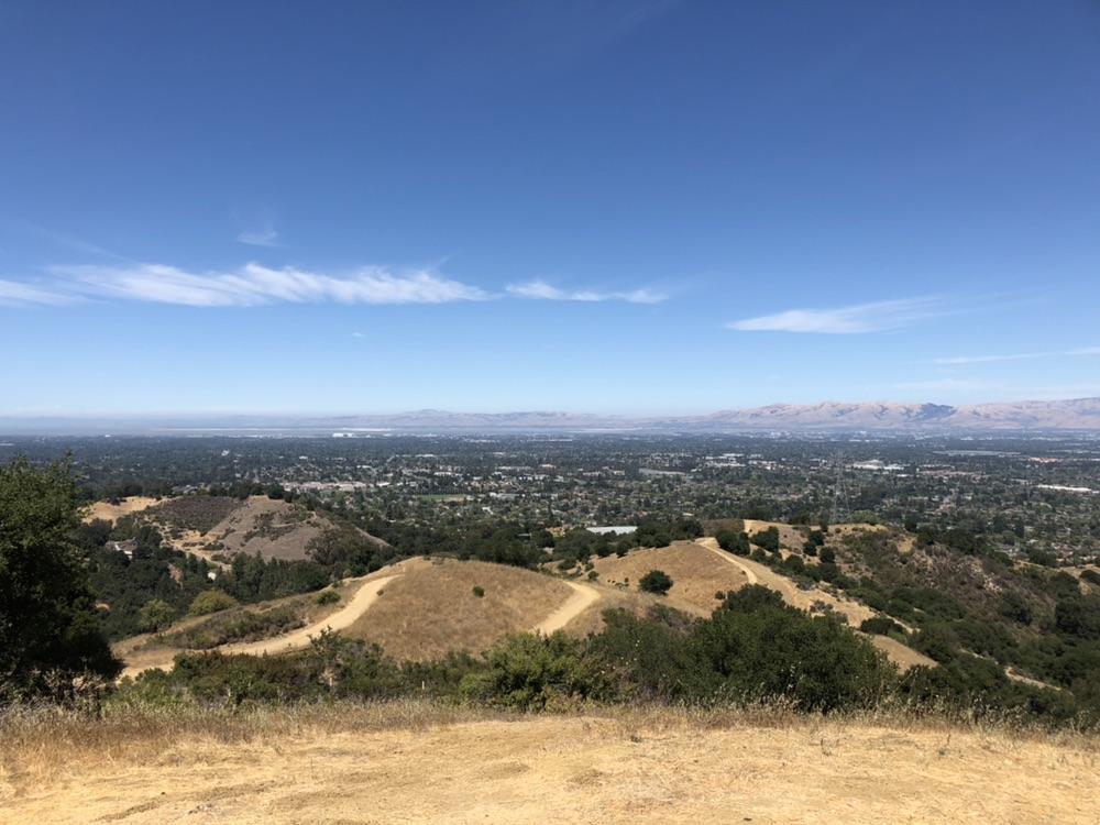 Expansive view of dry hills, a city, and distant mountains on a sunny day.