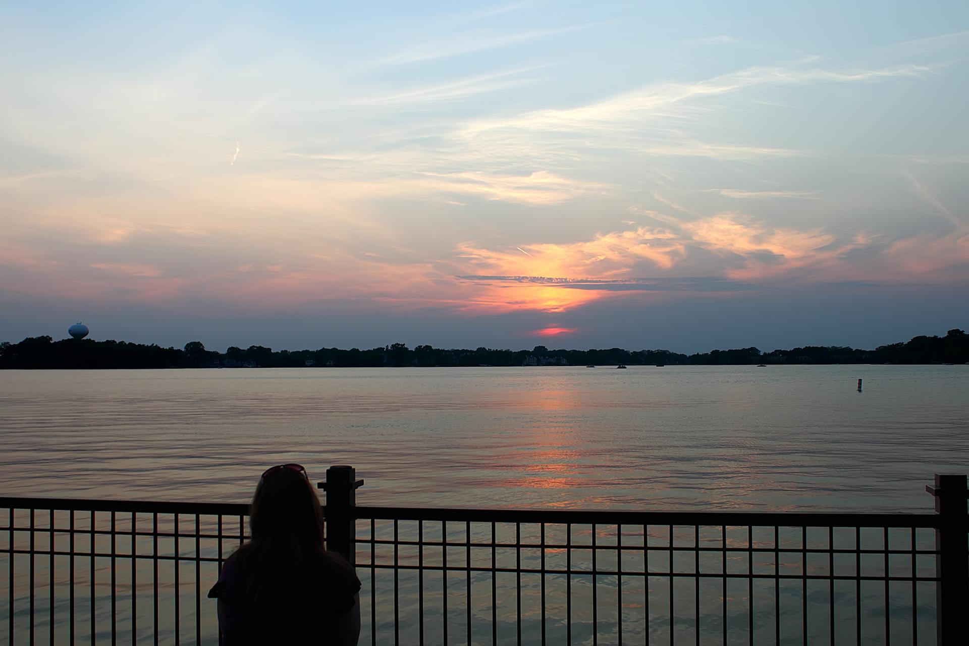 A person watches a vibrant sunset over a wide, calm lake.