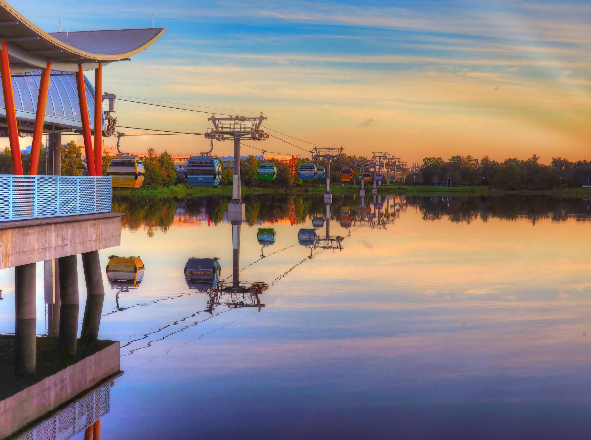Gondola lift system over calm water reflecting a colorful sunset sky.