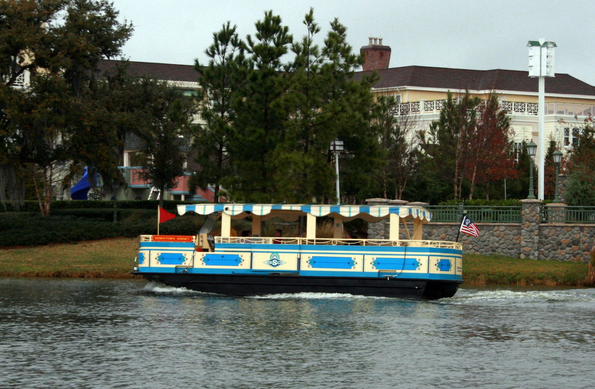 A blue and white boat with a striped canopy moves on water past a building. - Disney Springs loop via Willow Lake