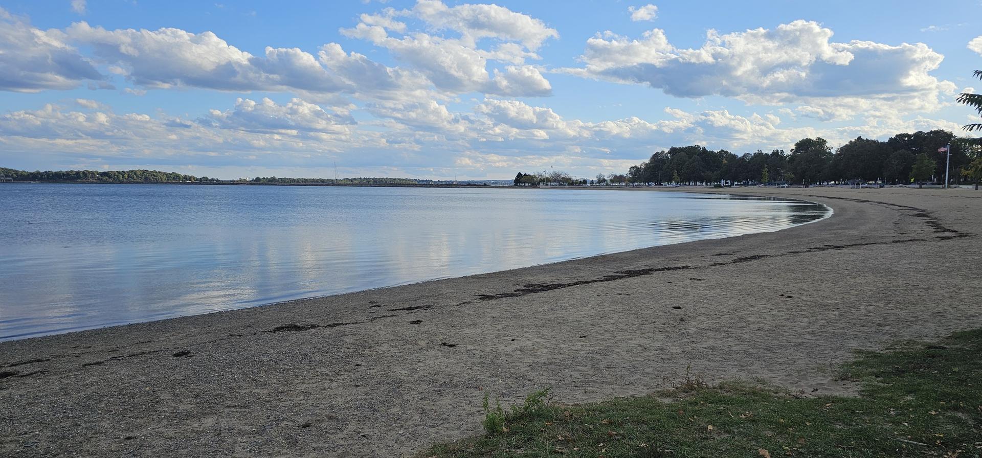 A wide, curving sandy beach meets calm water under a partly cloudy sky.