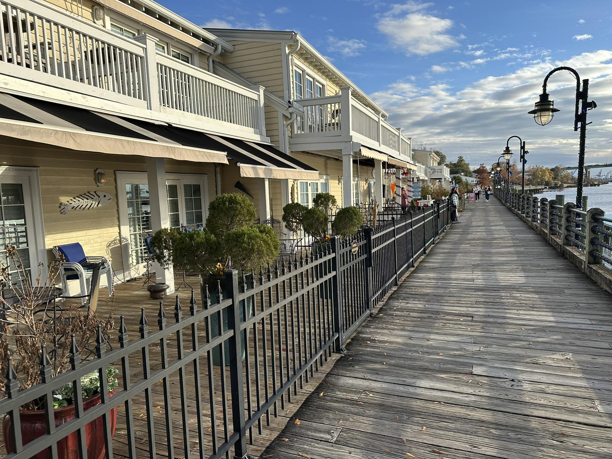 Waterfront boardwalk with yellow buildings and outdoor seating under a bright sky.