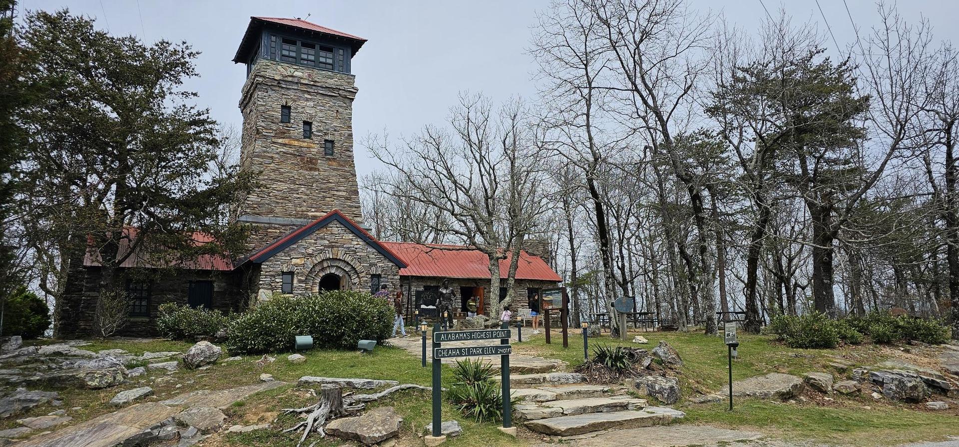 Stone tower building with red roof surrounded by bare trees, overcast day.
