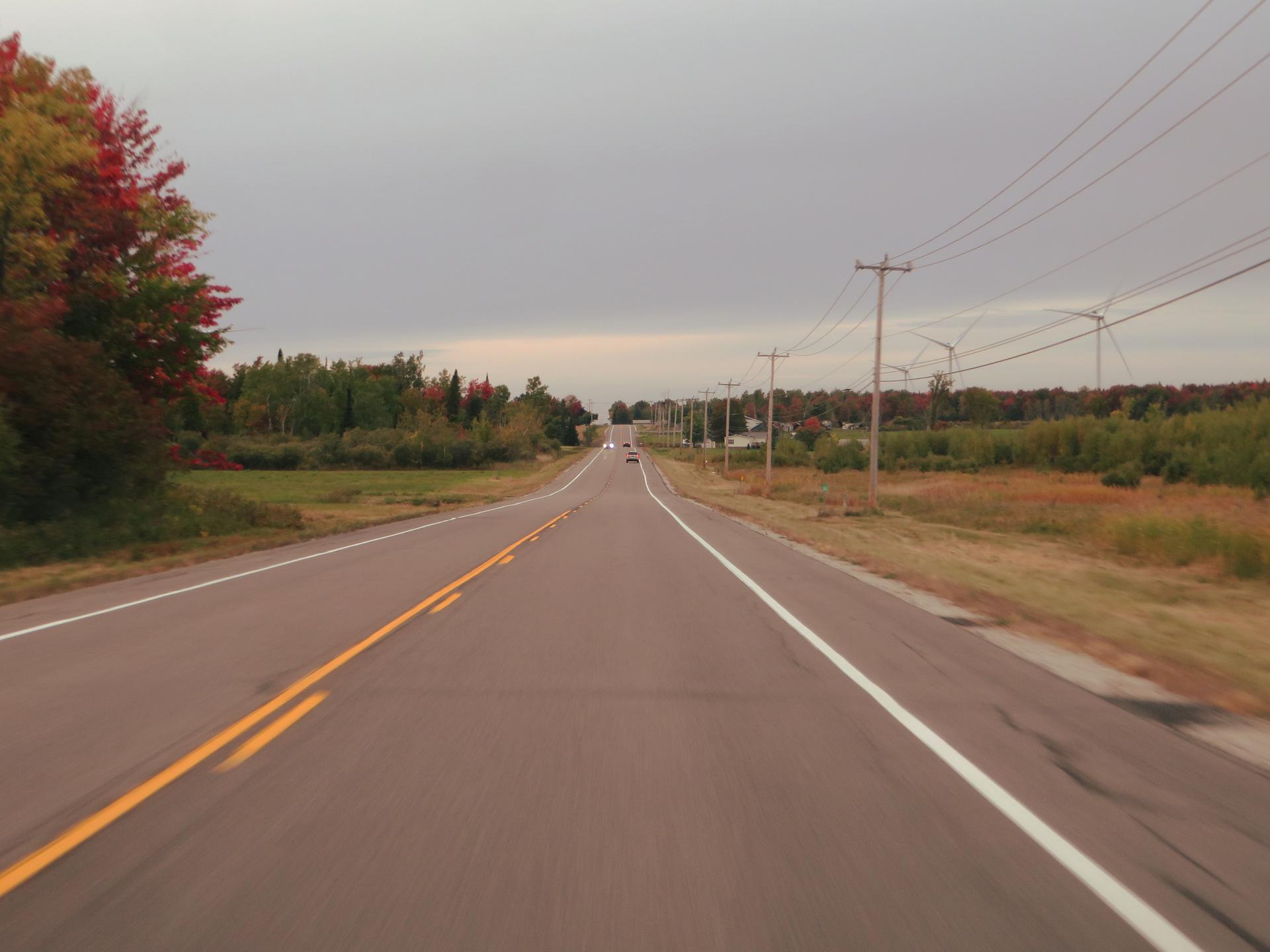 Long, empty rural road under an overcast sky with power lines.