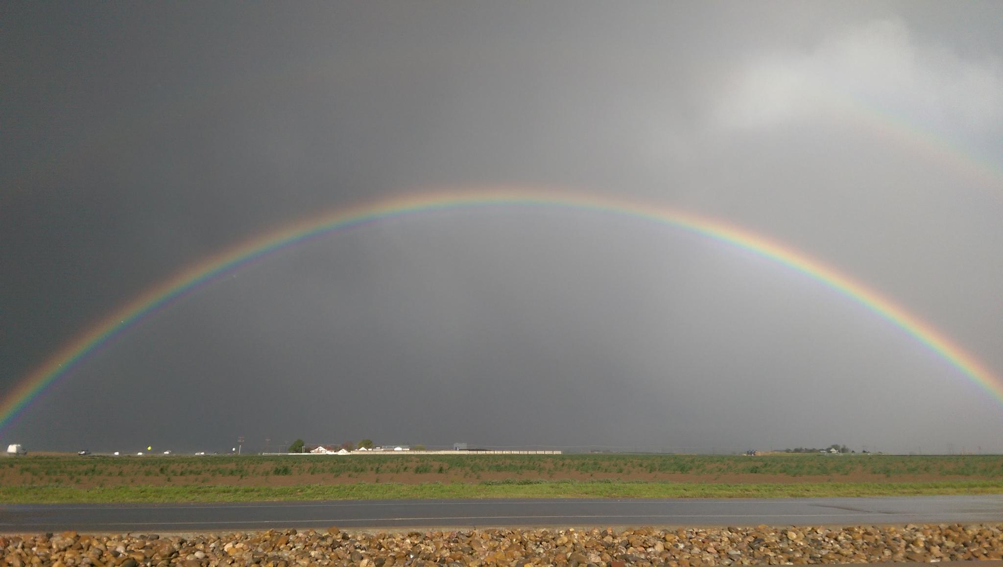 A vibrant rainbow arches over a dark, stormy sky and green field.