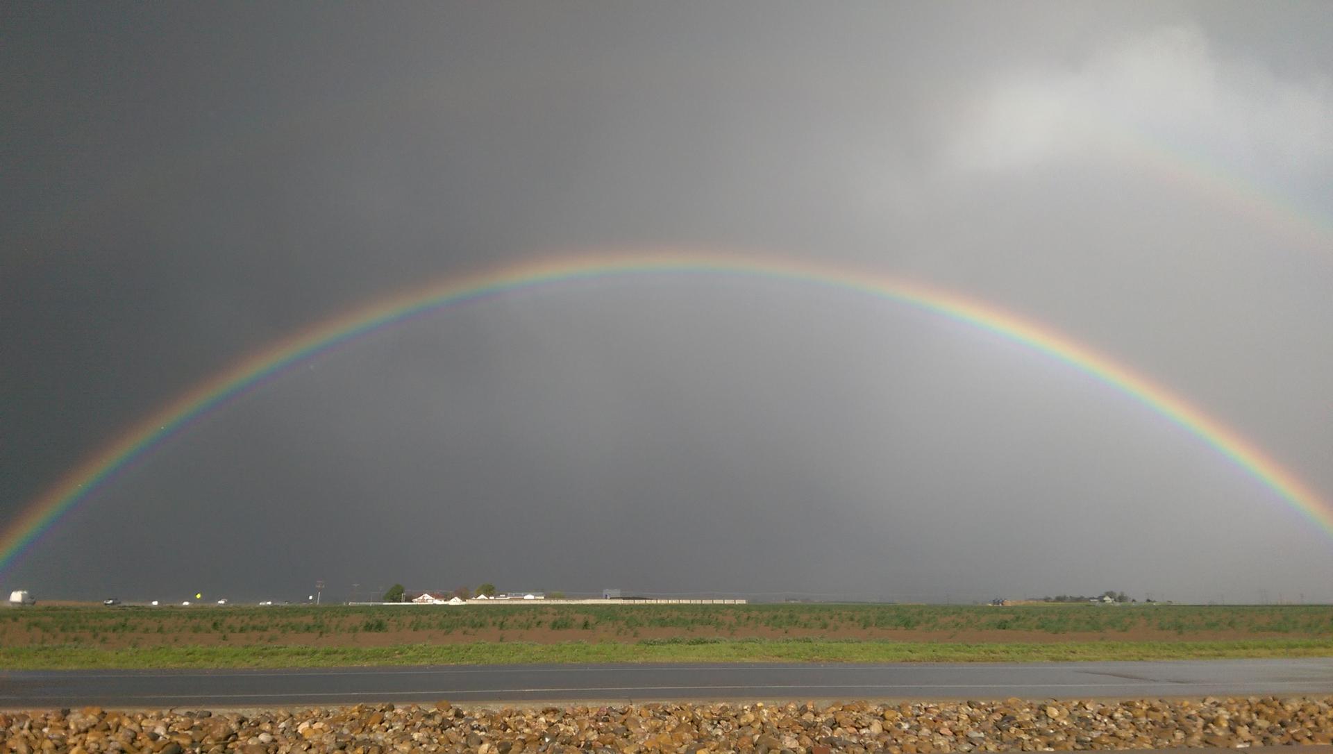 A vibrant rainbow arches over a dark, stormy sky and green field.