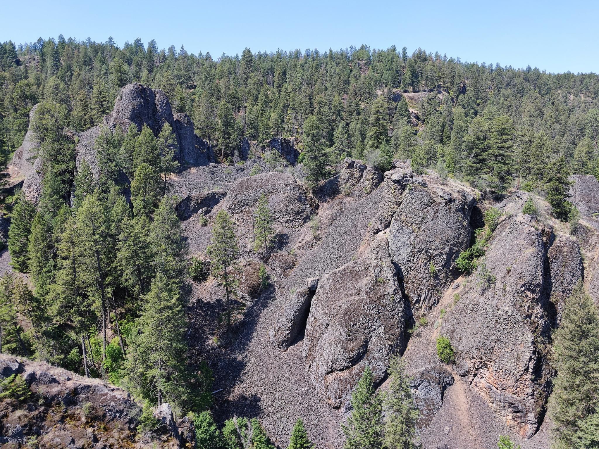 Sunlit, rugged landscape with dark rock formations and dense green forest. - Deep Creek and Spokane River Centennial Loop