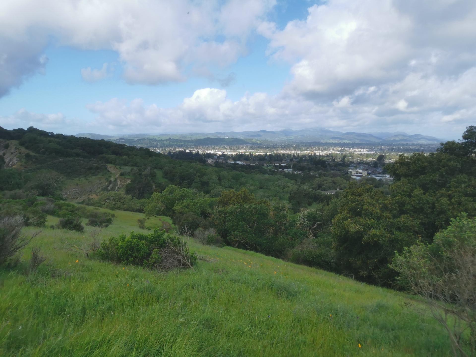 Green hillside overlooking a distant town under a partly cloudy sky.