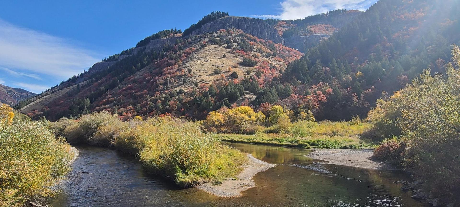 Sunny autumn day, river winding through a valley with colorful mountains.