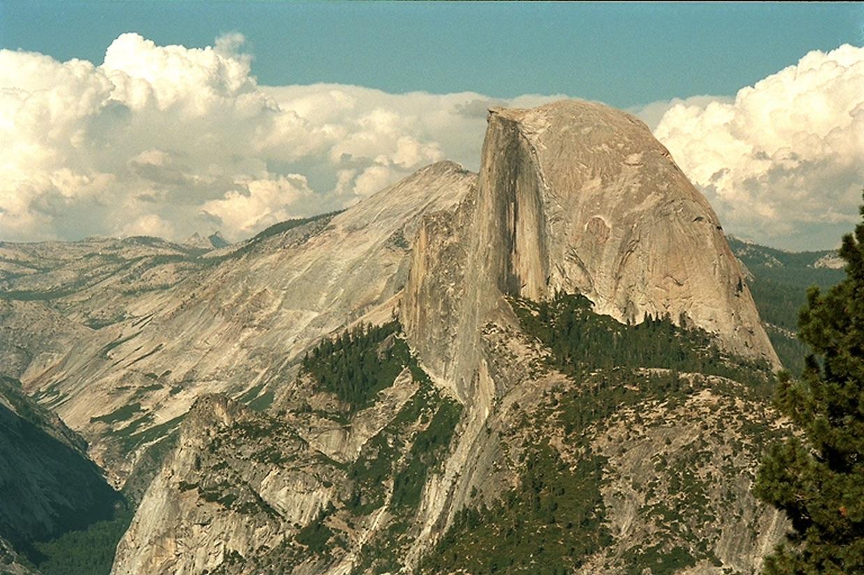 A large granite dome and surrounding mountains under a partly cloudy sky.