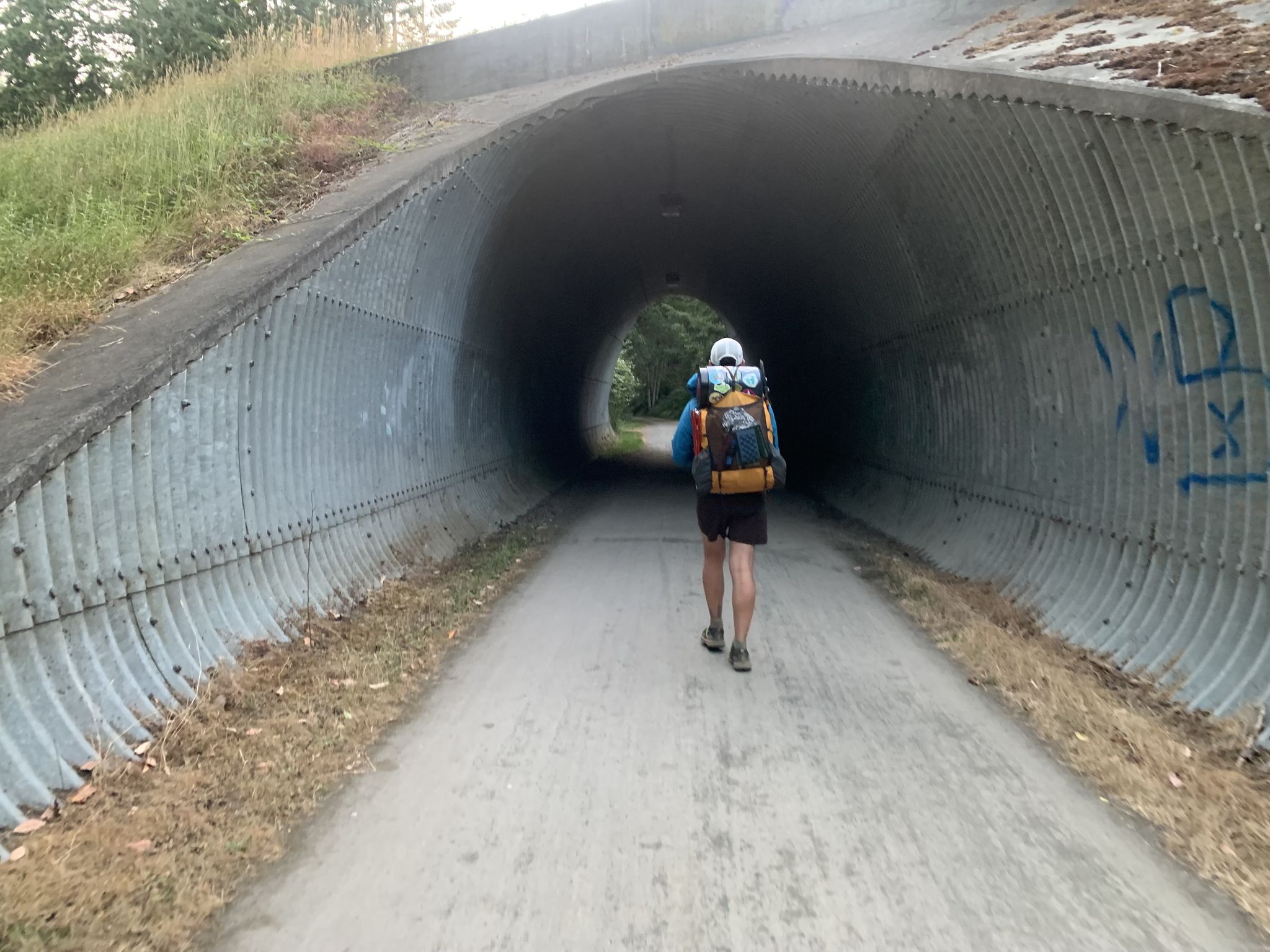 A person with a large backpack walks through a long, concrete tunnel. - Port Townsend loop
