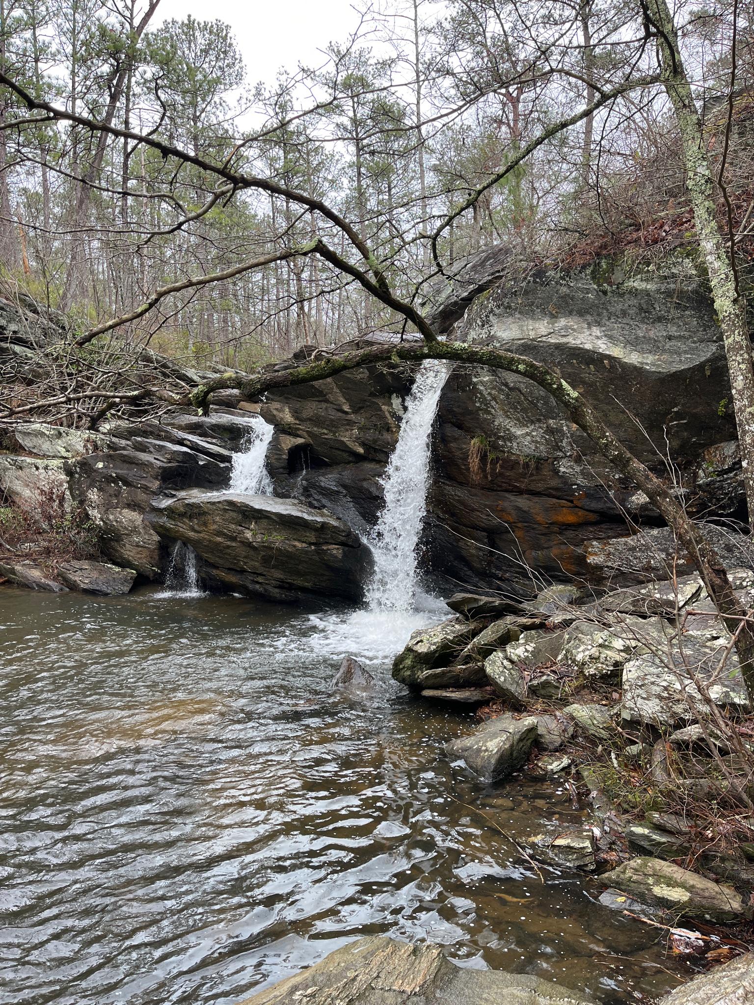 Two waterfalls cascade over dark rocks into a pool under an overcast sky.