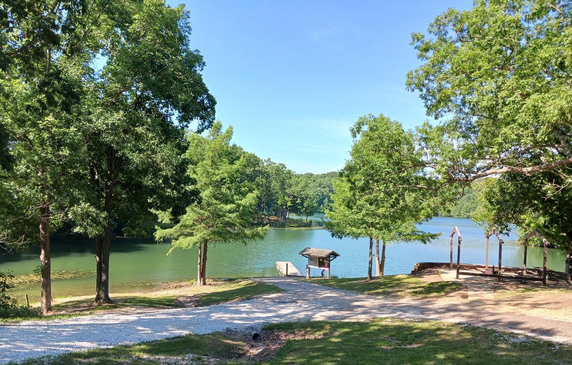Sunny lake view framed by trees, with a path leading to a small dock.