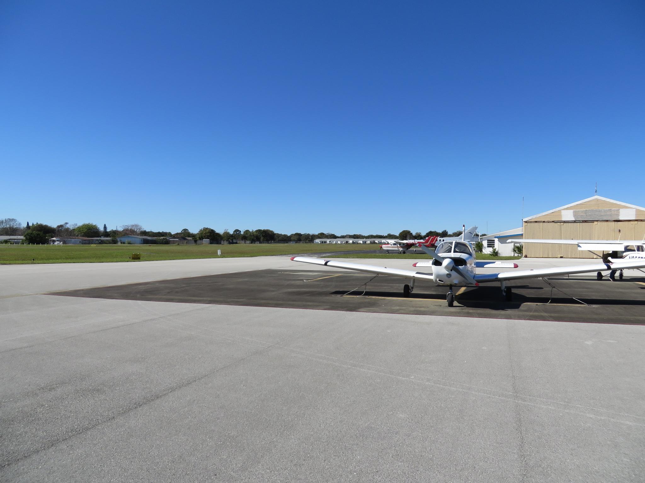 Small white airplane parked on an airfield tarmac under a clear blue sky.