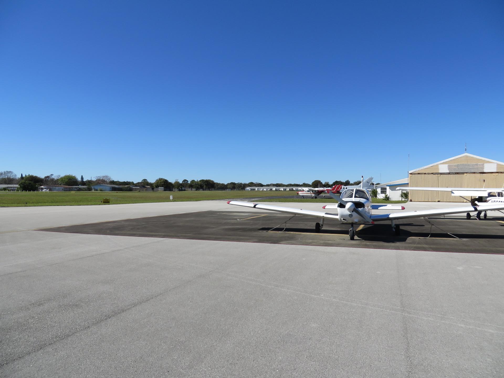 Small white airplane parked on an airfield tarmac under a clear blue sky.
