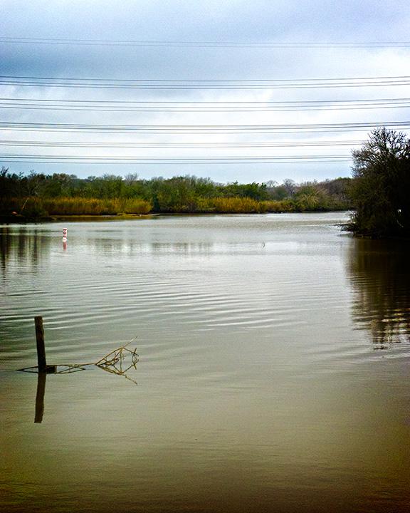 Wide river under an overcast sky with distant trees and power lines.