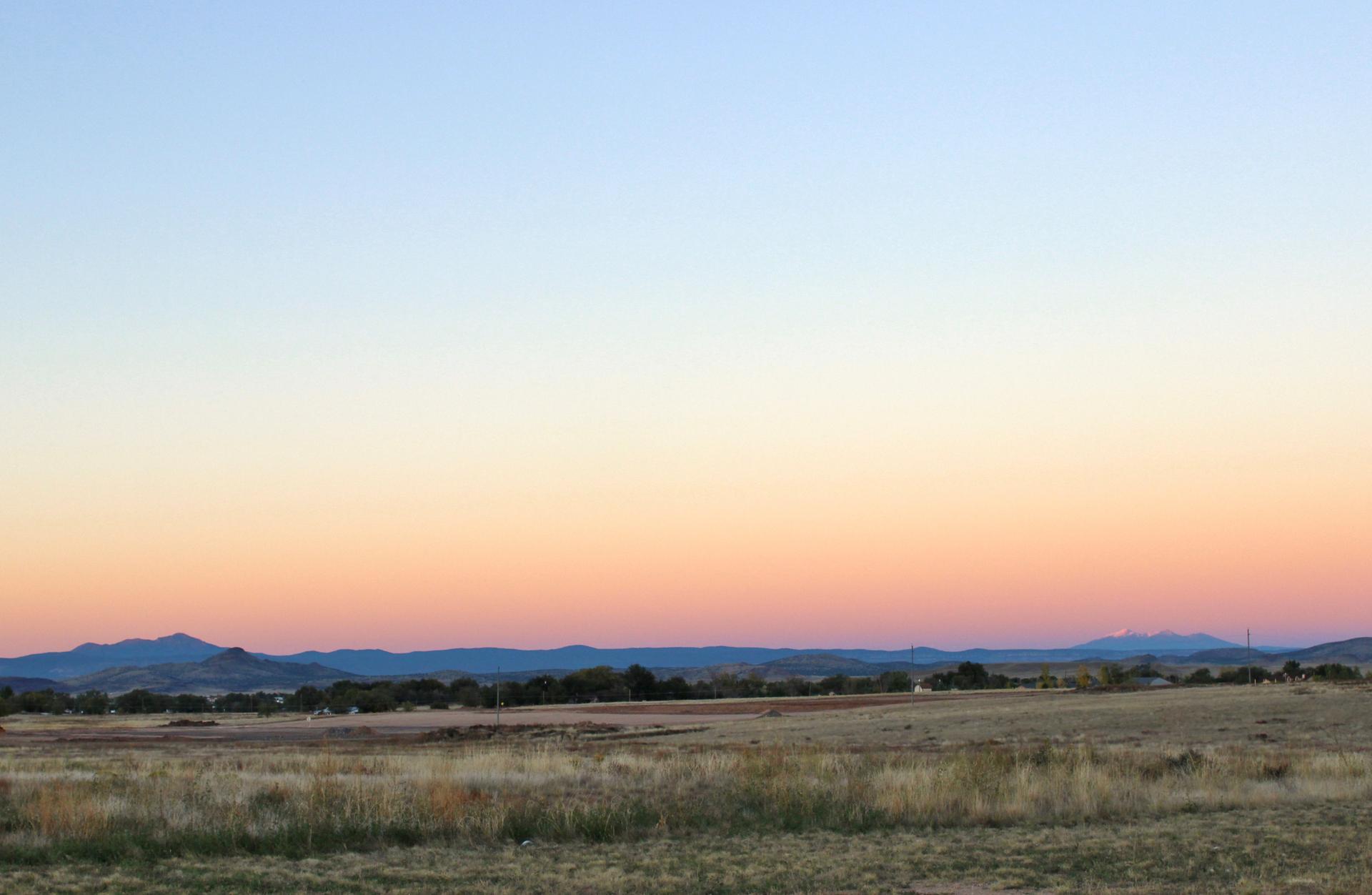 Expansive landscape at dusk with a gradient sky over fields and distant mountains.