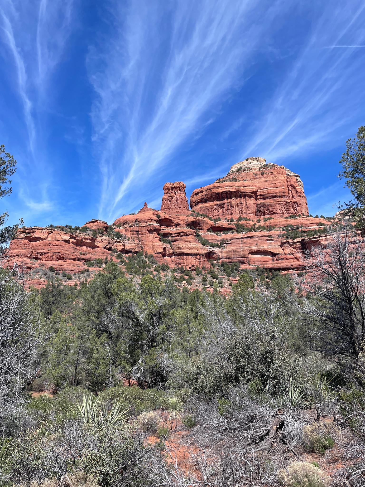 Majestic red rock formations under a vibrant blue sky with wispy clouds.