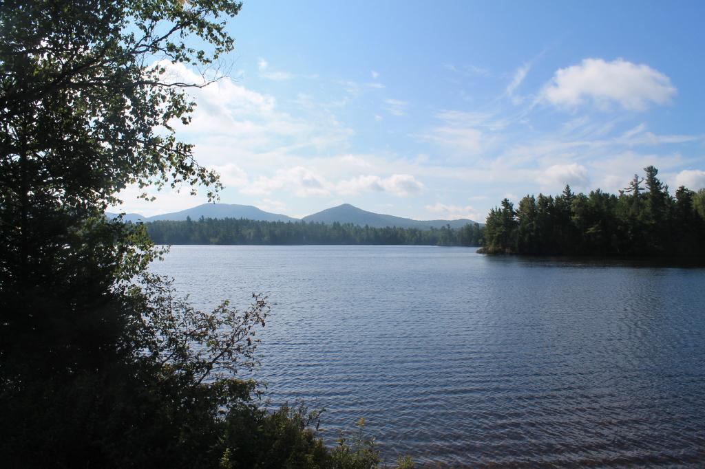 Calm lake with distant mountains under a bright, partly cloudy sky.