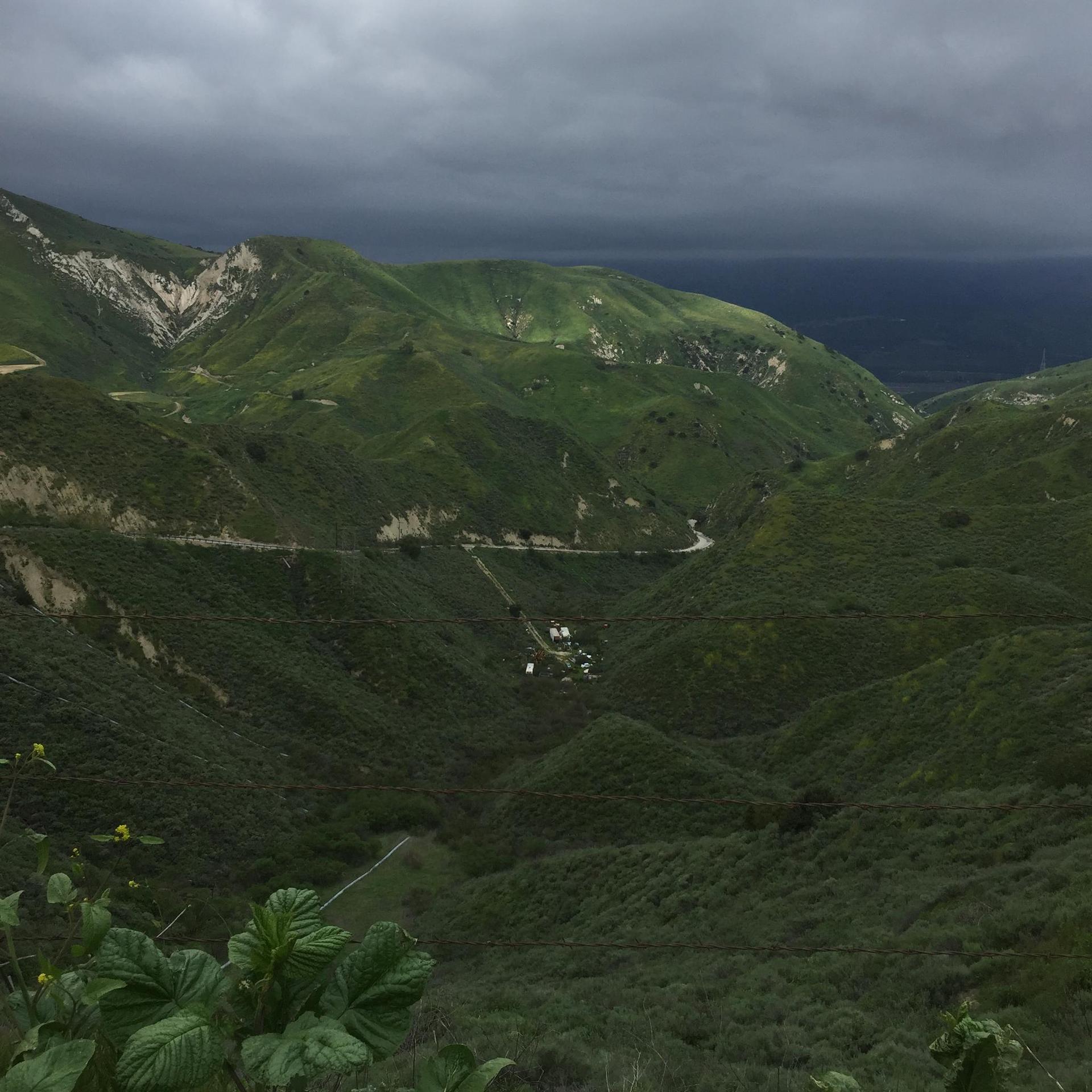 Dark, cloudy sky over lush green rolling hills and deep valleys.