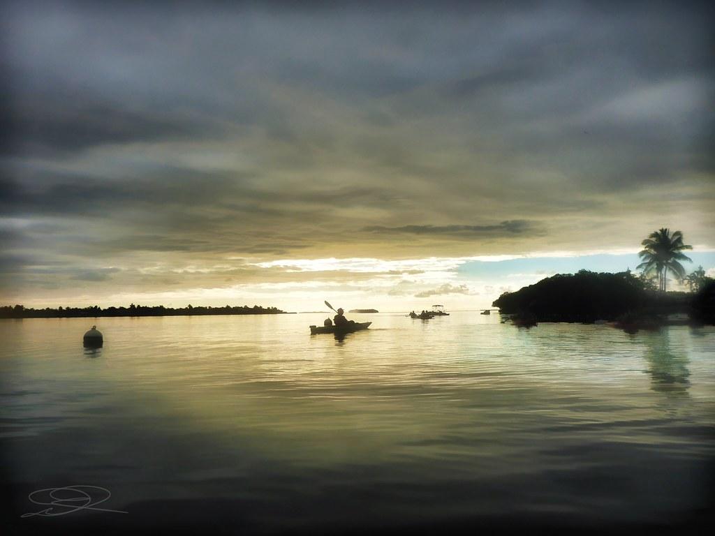 A kayaker paddles on calm water under a dramatic, cloudy, low-light sky.
