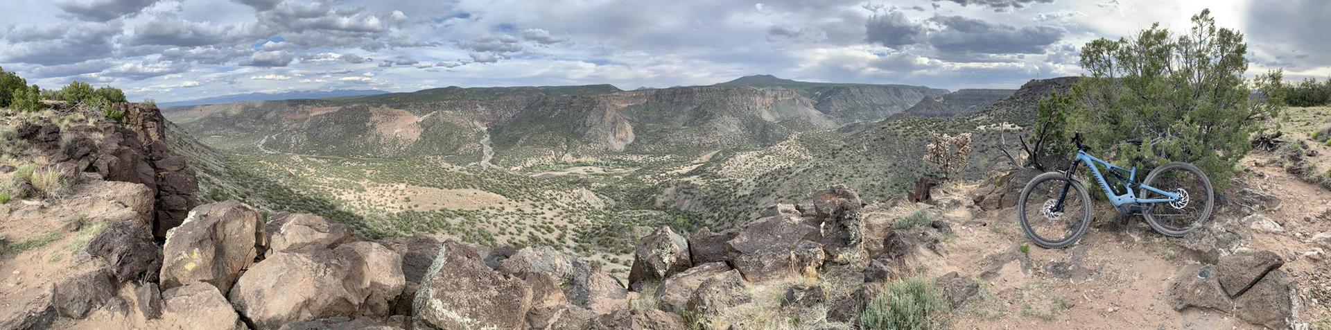 Mountain bike parked on a rocky cliff overlooking a vast canyon under cloudy skies.