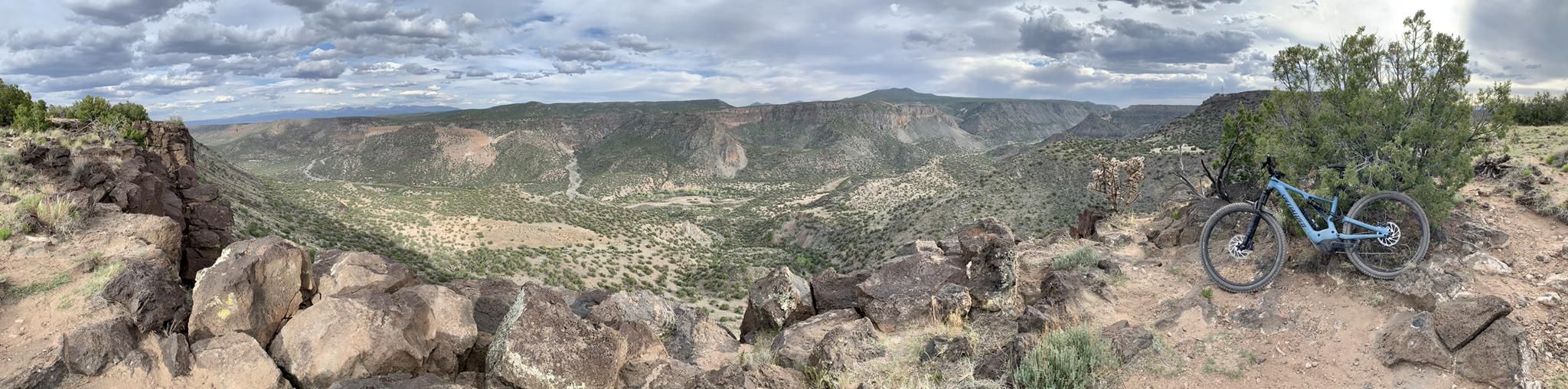Mountain bike parked on a rocky cliff overlooking a vast canyon under cloudy skies. - Potrillo Canyon Loop Trail