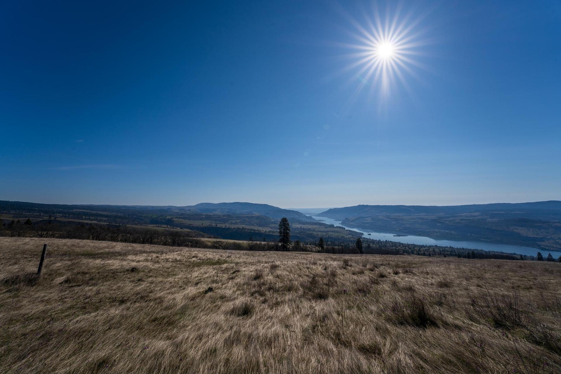 A vast dry grassy field overlooks distant mountains and a wide river.