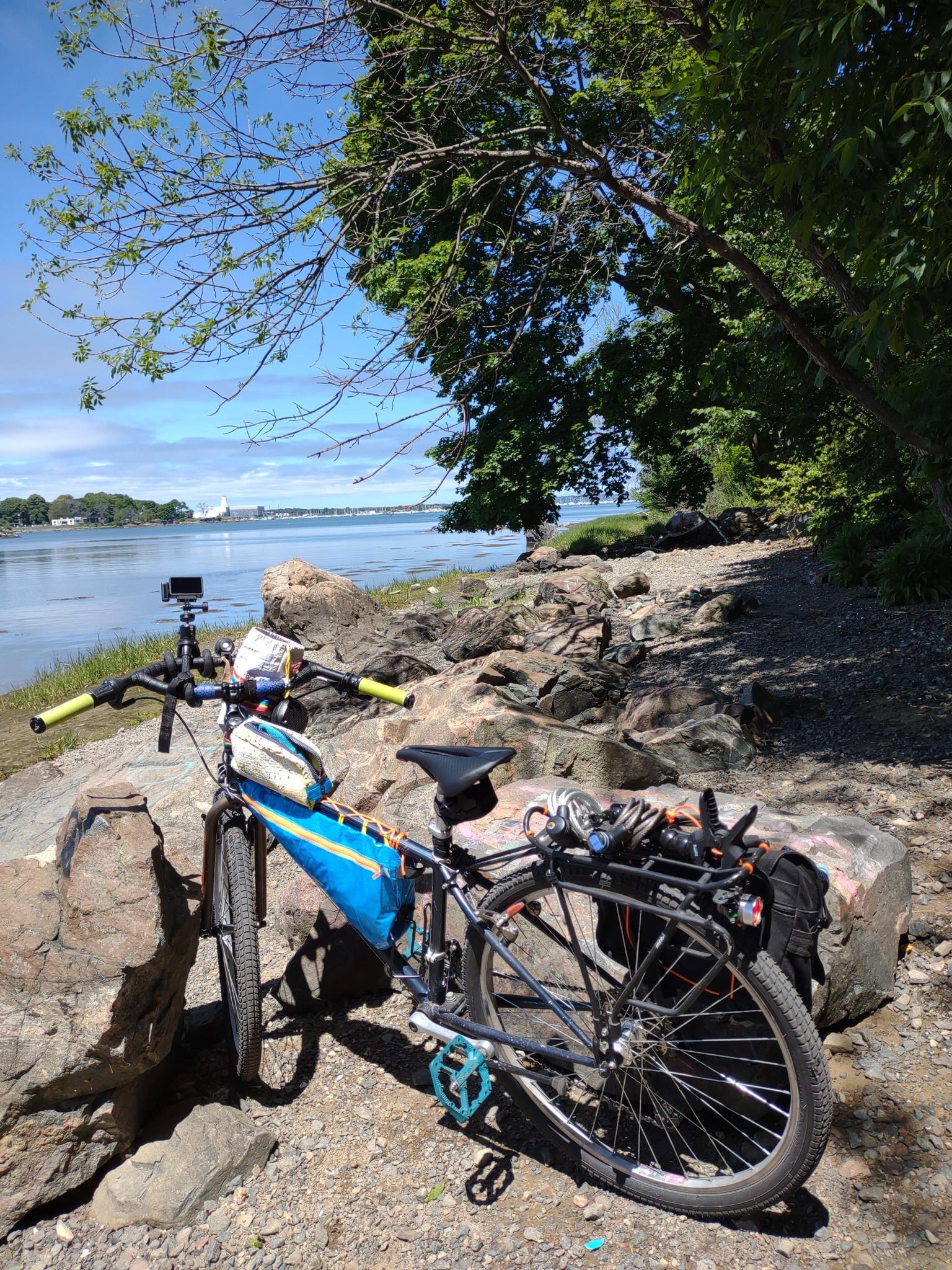 Bicycle parked on a rocky shore beside calm water under a sunny sky.