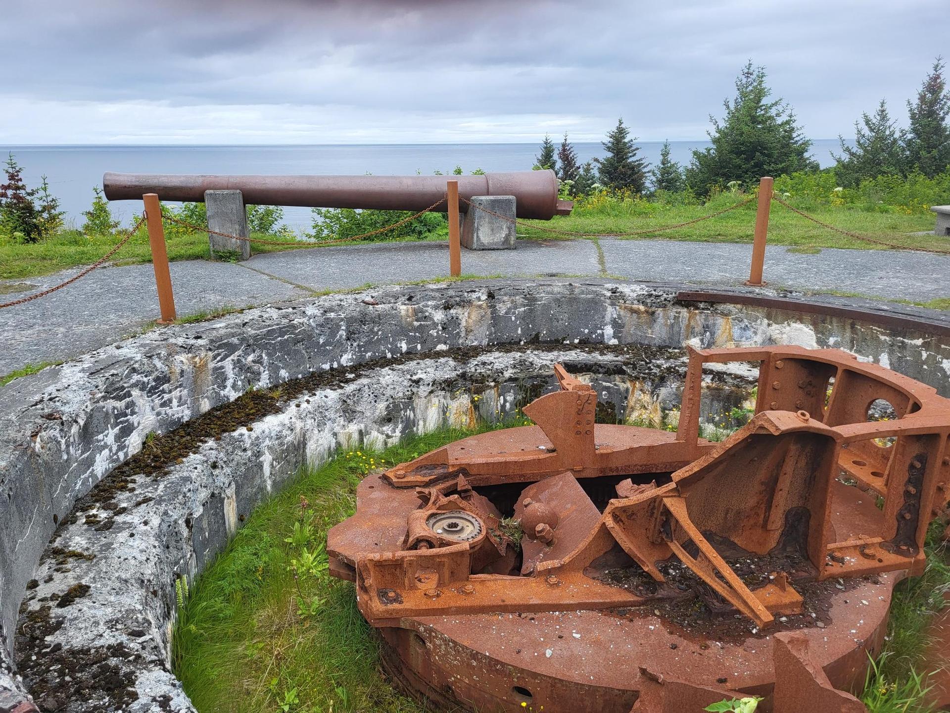 Old cannon and rusty machinery overlooking the ocean on a cloudy day.