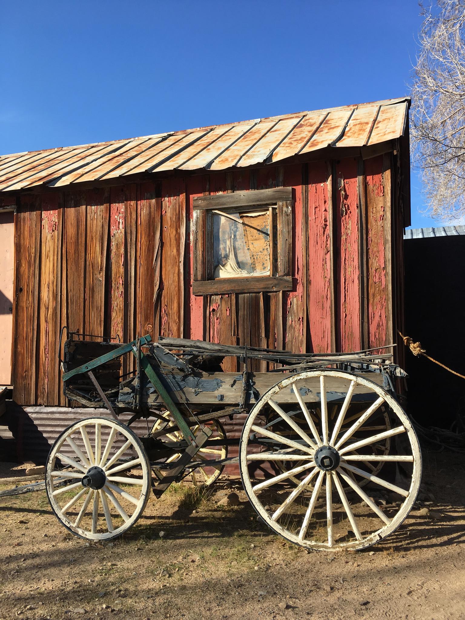 An antique wooden wagon in front of an old red wooden building.