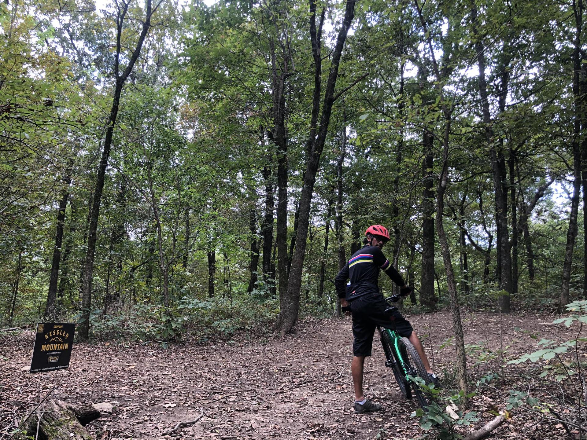 Mountain biker standing with bike on a dirt path in a dense green forest.