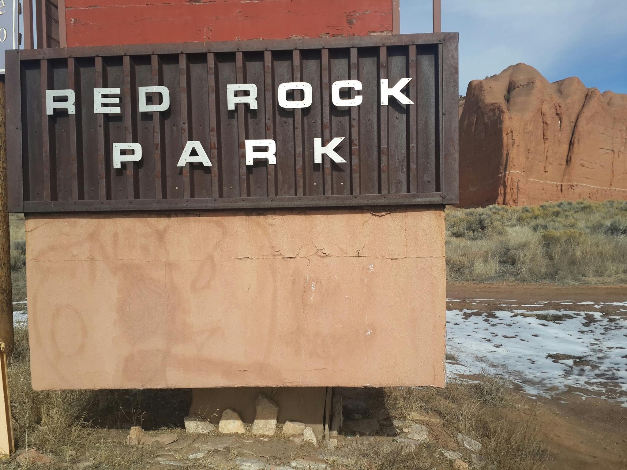 A wooden sign with 'RED ROCK PARK' text, with red rock formations behind.