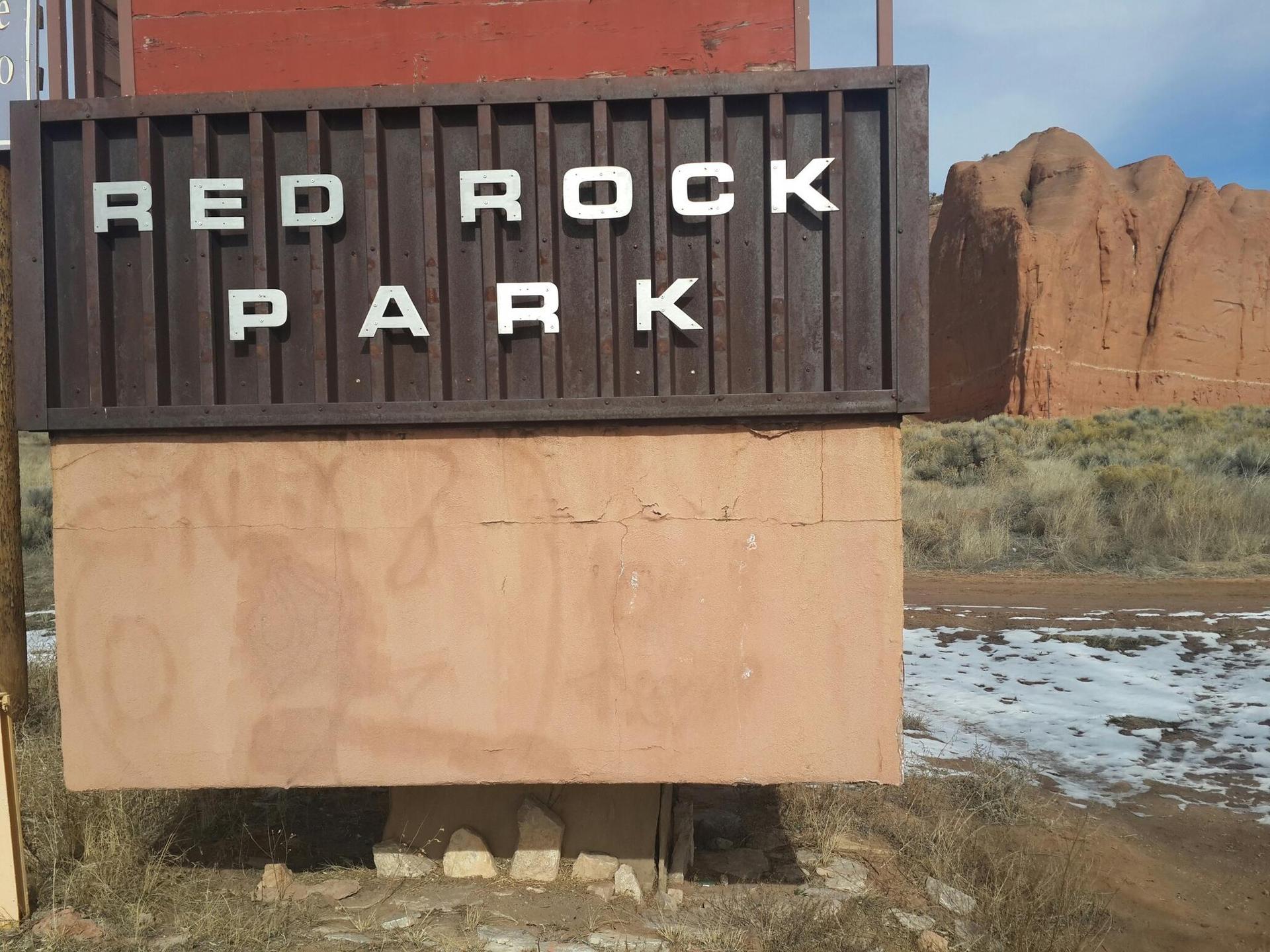 A wooden sign with 'RED ROCK PARK' text, with red rock formations behind.