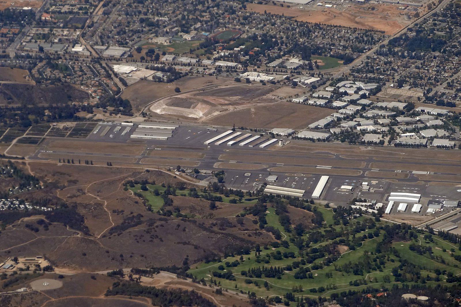 Aerial view of an airfield, urban buildings, green golf course, and dry hills.