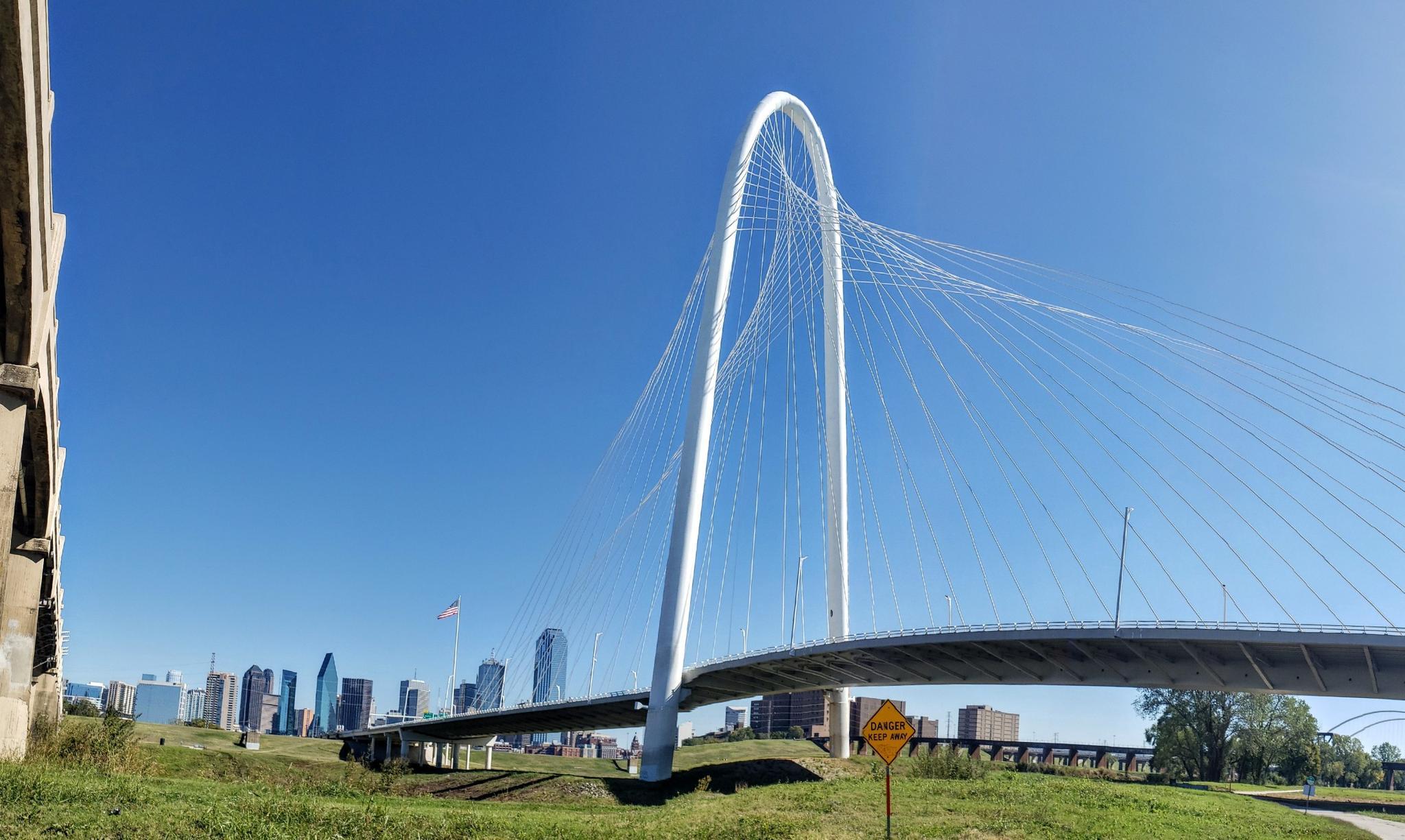Modern white arch bridge against a clear blue sky with a city skyline.