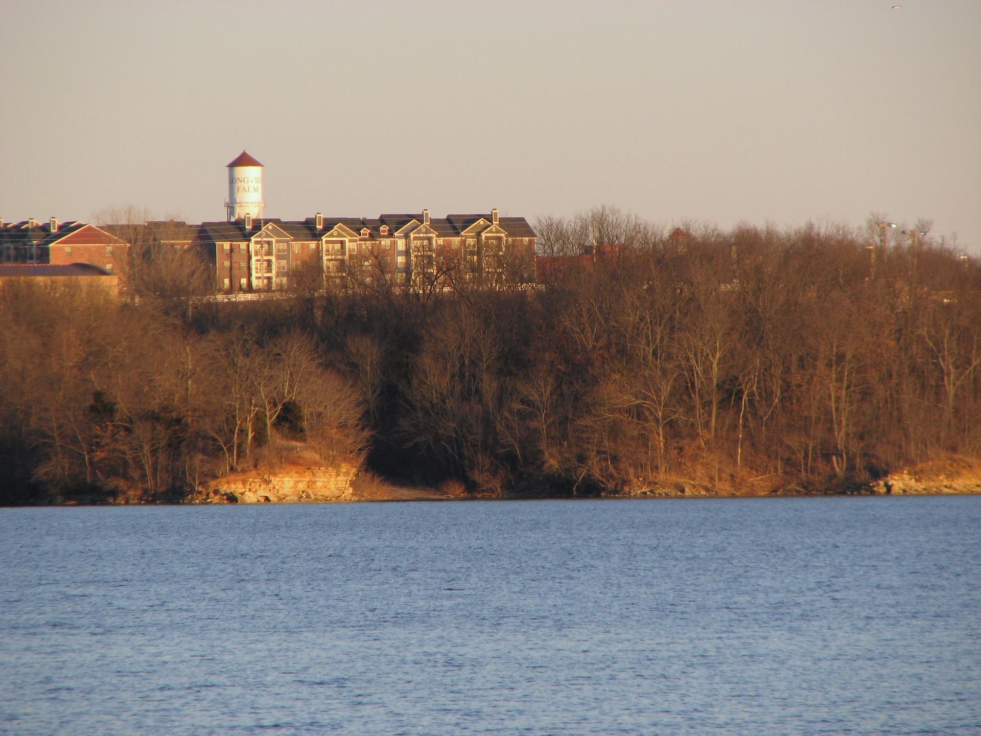 Water tower and buildings overlooking a lake with bare trees in warm light.