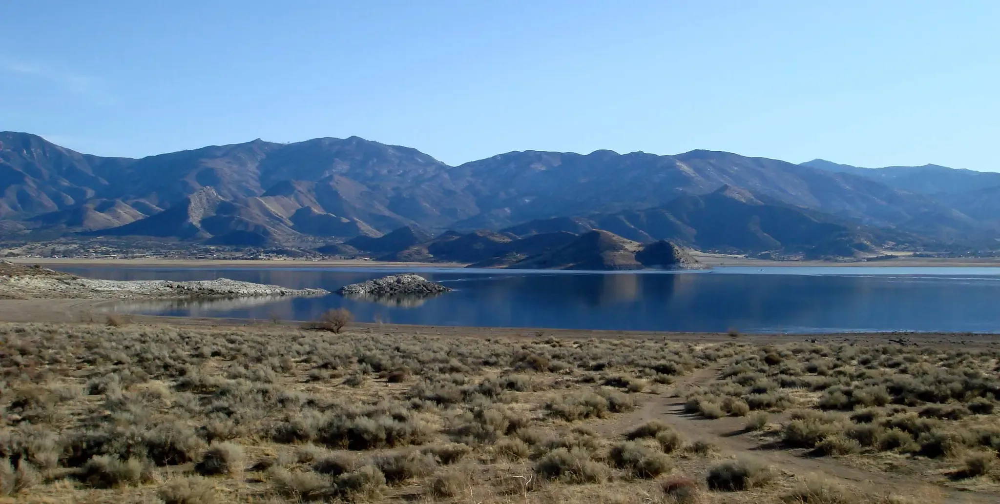 Calm lake with dry brush and rugged mountains under a clear blue sky. - Lake Isabella and Silver City Ghost Town loop
