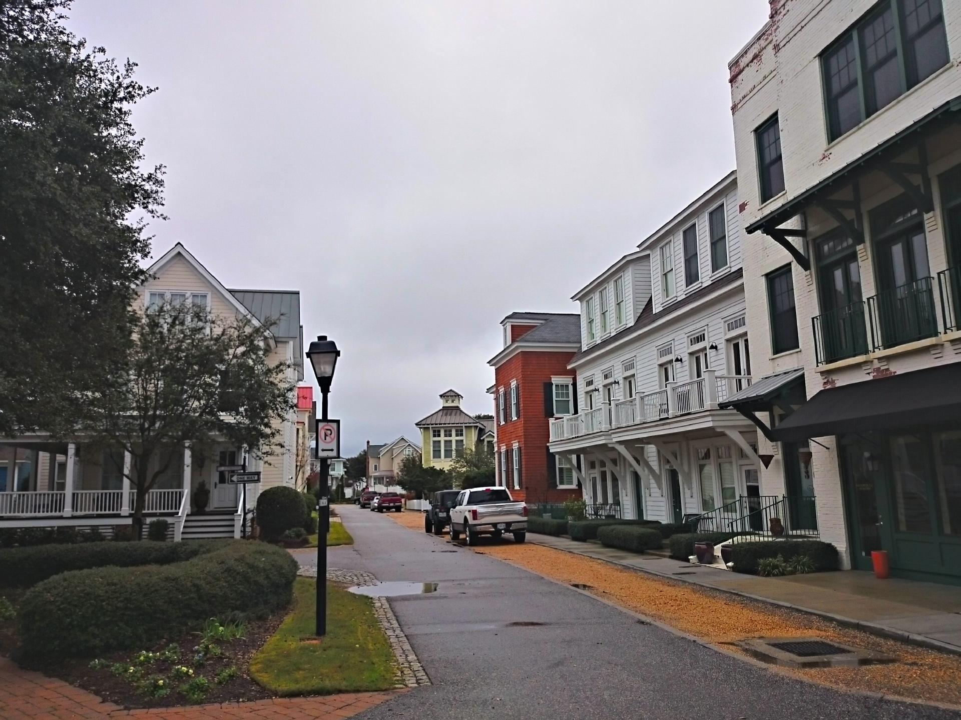 Overcast street scene with colorful houses, parked cars, and a lamppost.
