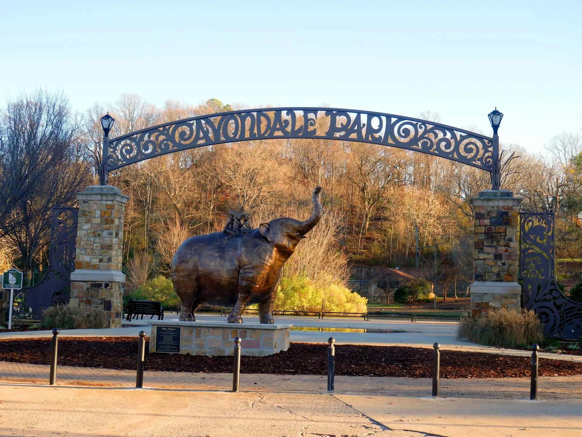 A large bronze elephant statue stands under an ornate park archway.