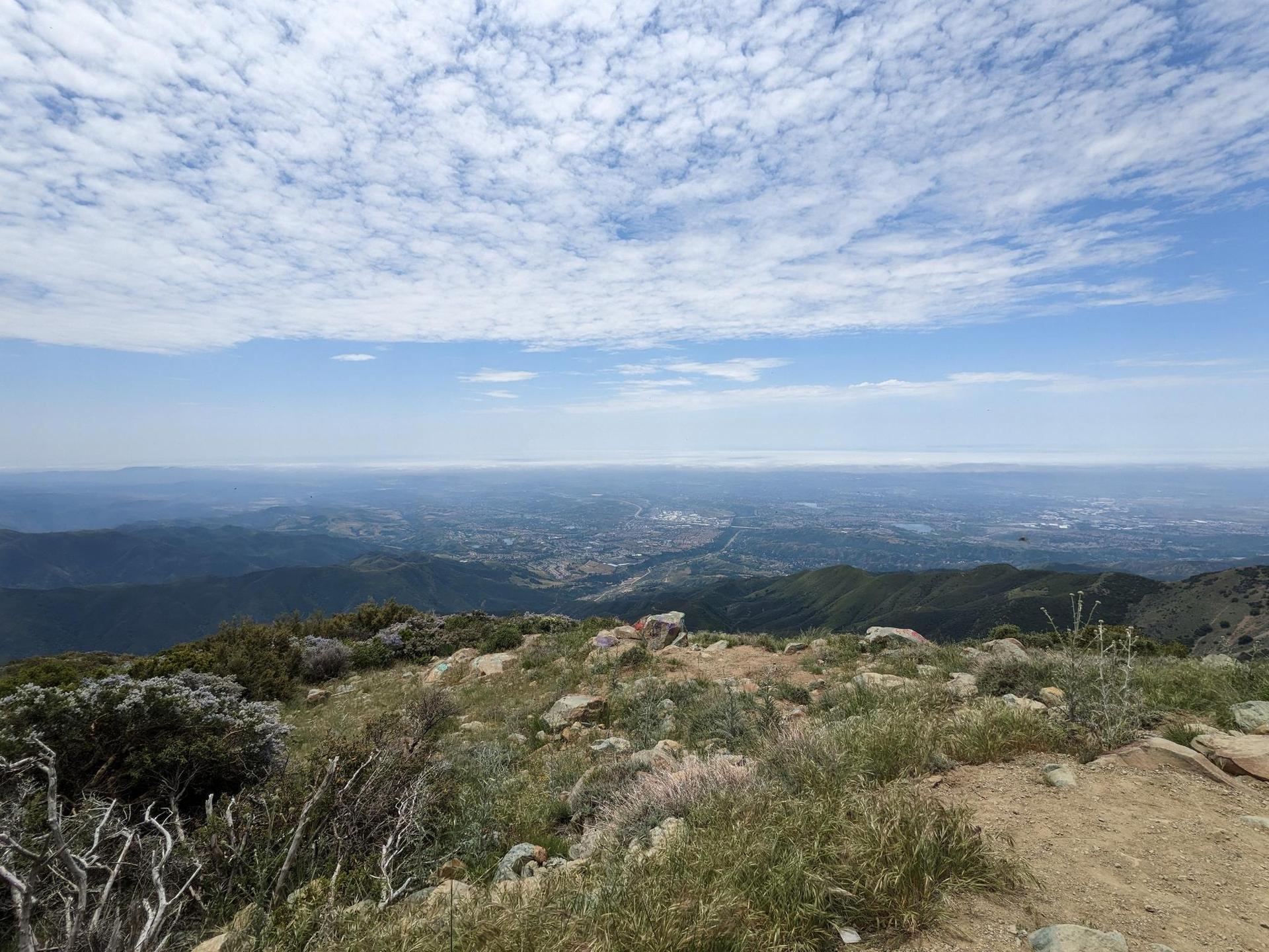Panoramic view from a rocky mountain peak overlooking a distant city under clouds.