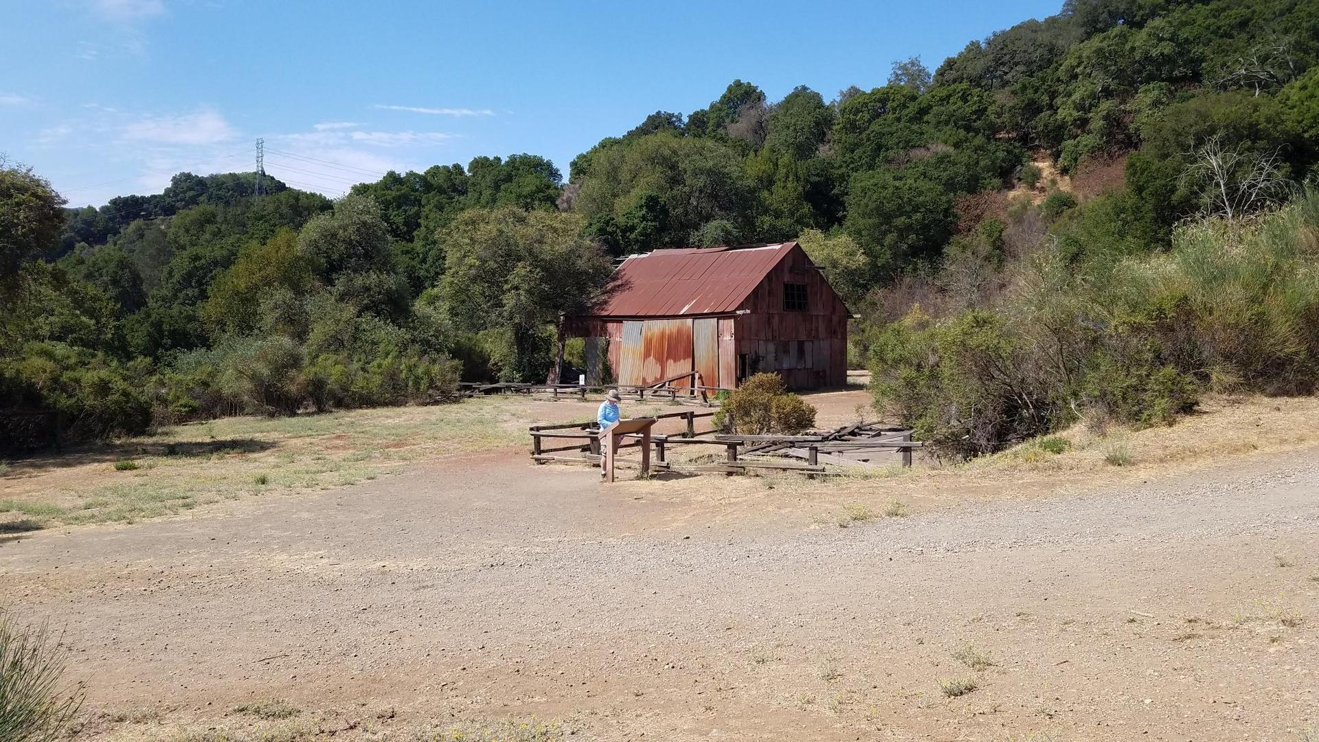 Sunny view of a person near an old barn surrounded by green hills.