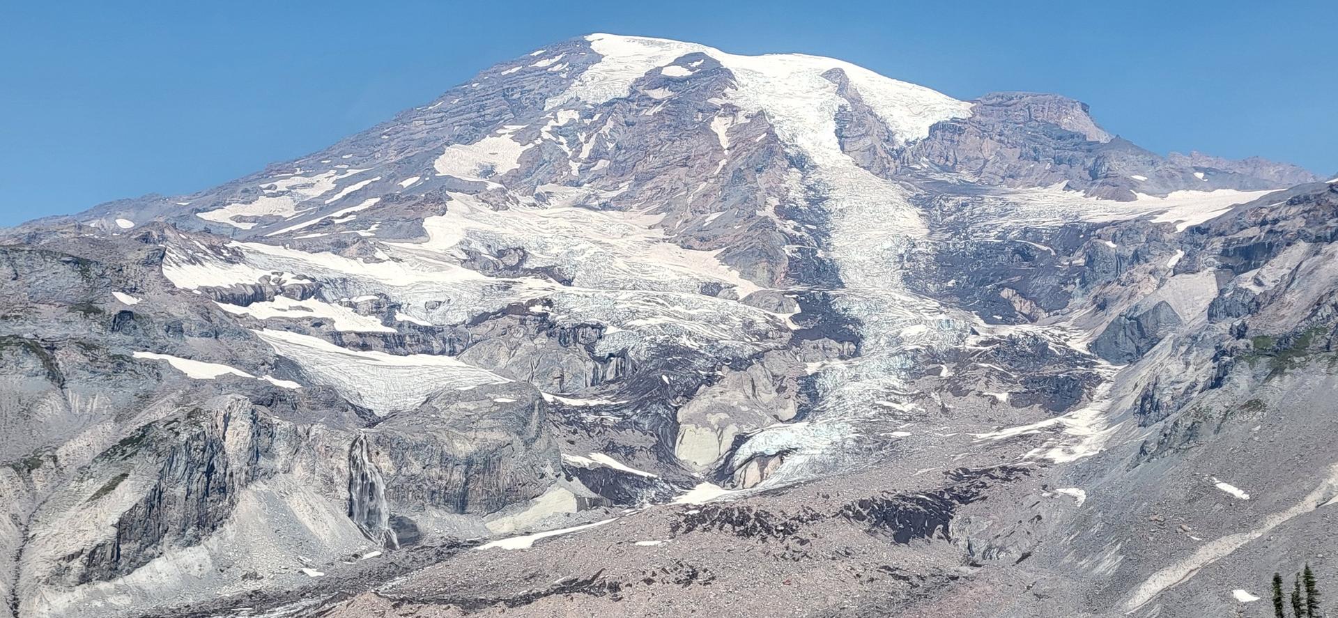 Expansive view of a snow-covered mountain with multiple glaciers and rocky terrain.