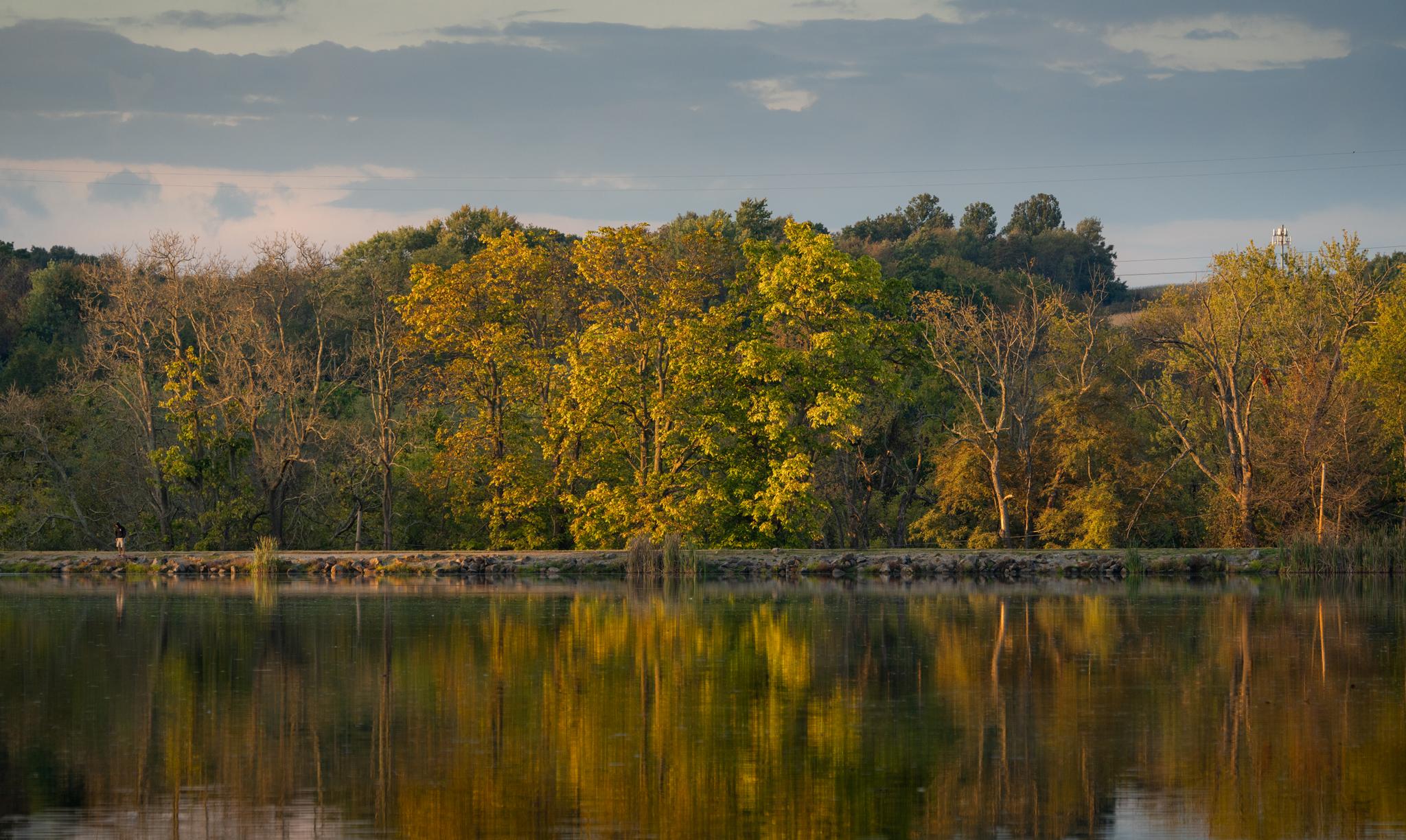Calm lake reflecting colorful autumn trees under a partly cloudy sky.