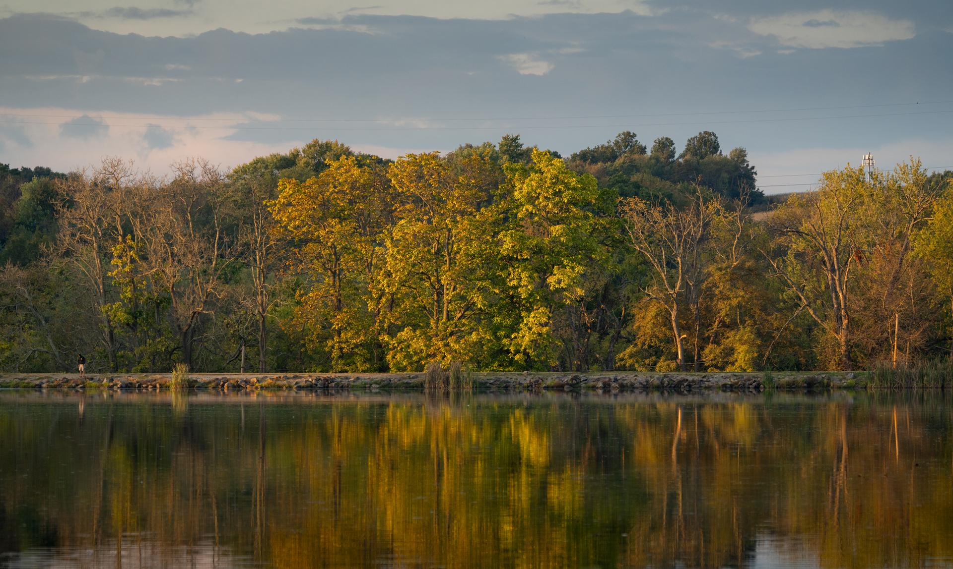 Calm lake reflecting colorful autumn trees under a partly cloudy sky.
