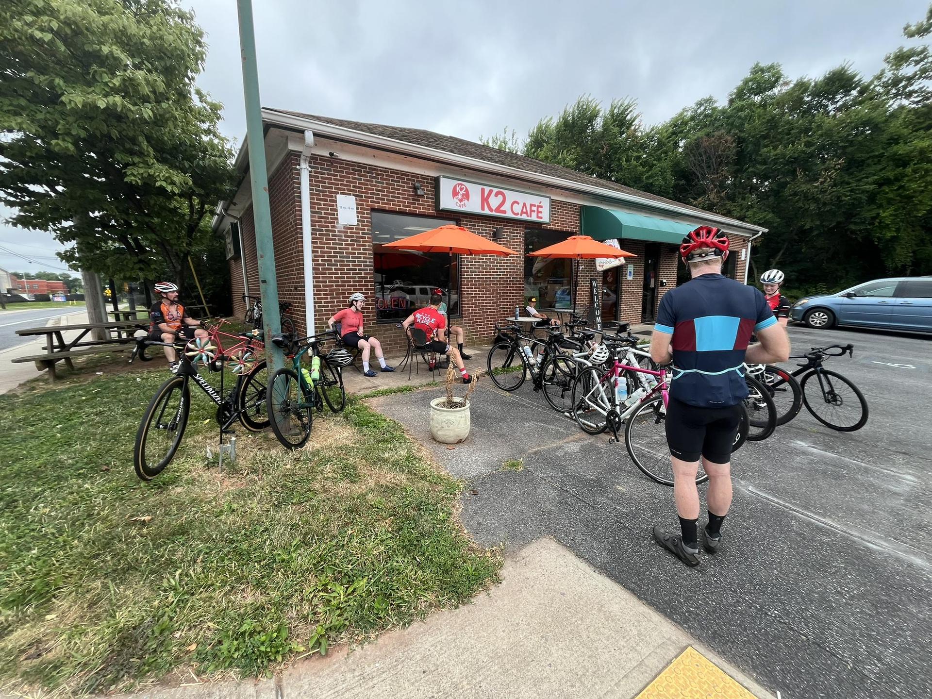 Cyclists gather with bikes outside a cafe on an overcast day.