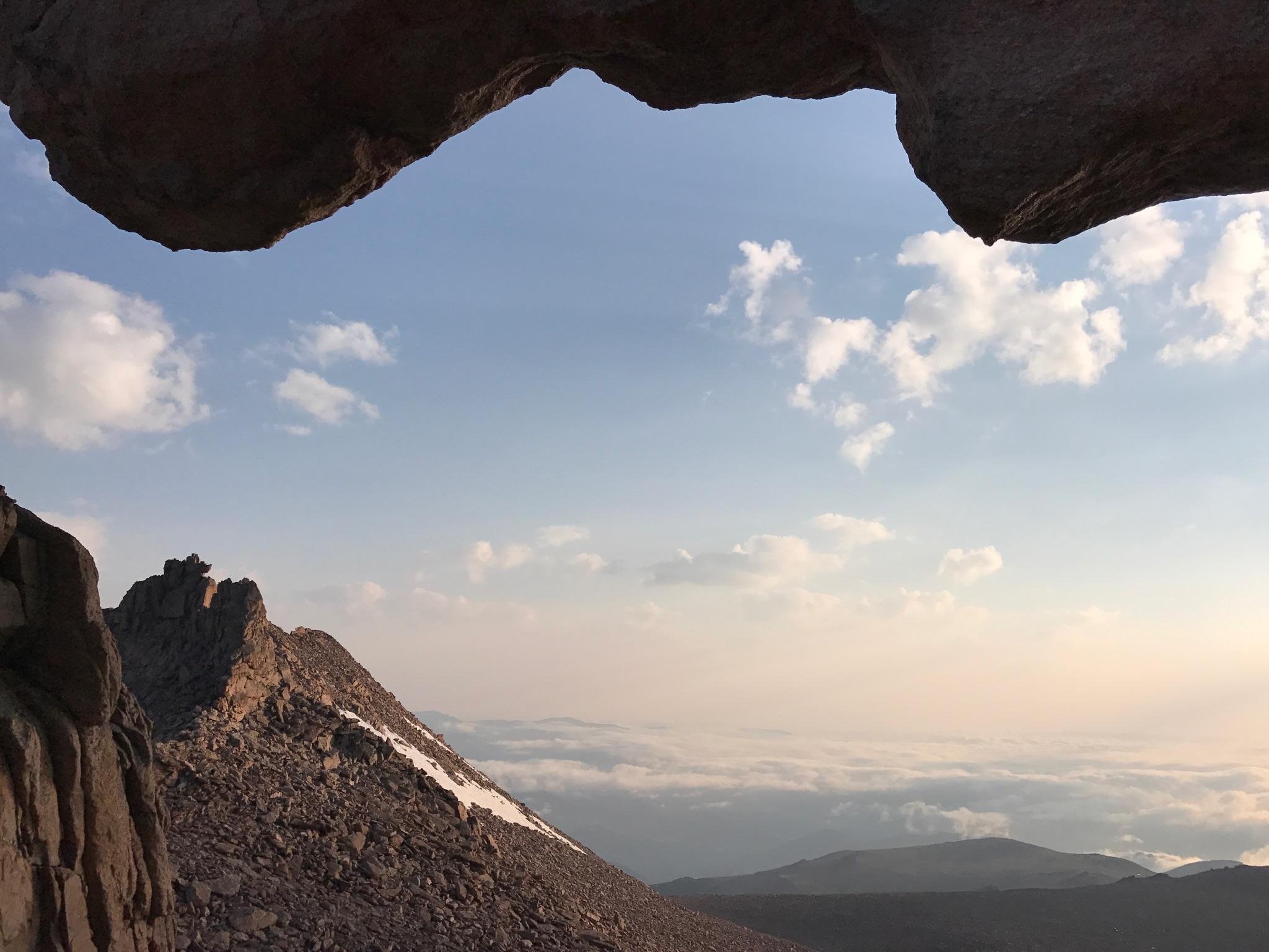 View of a rocky mountain peak and distant clouds through a rock arch.