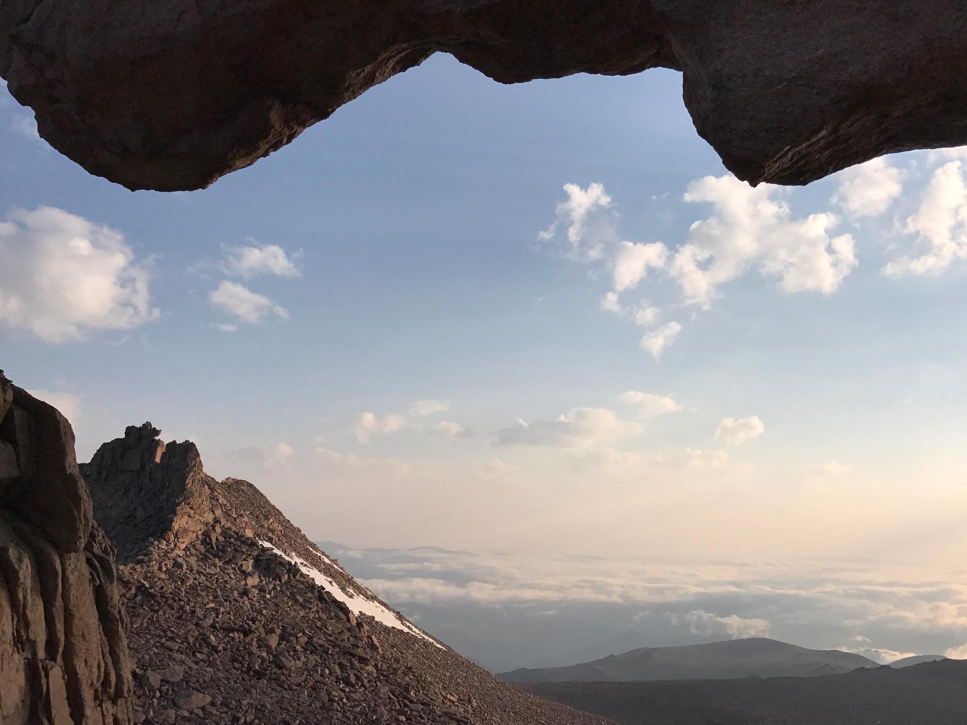 View of a rocky mountain peak and distant clouds through a rock arch.