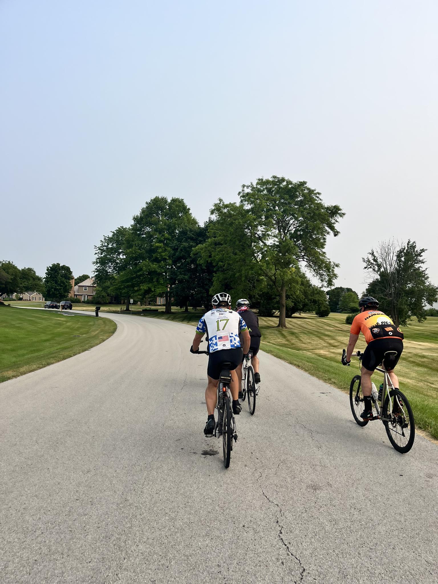 Three cyclists ride on a paved road through a green landscape.