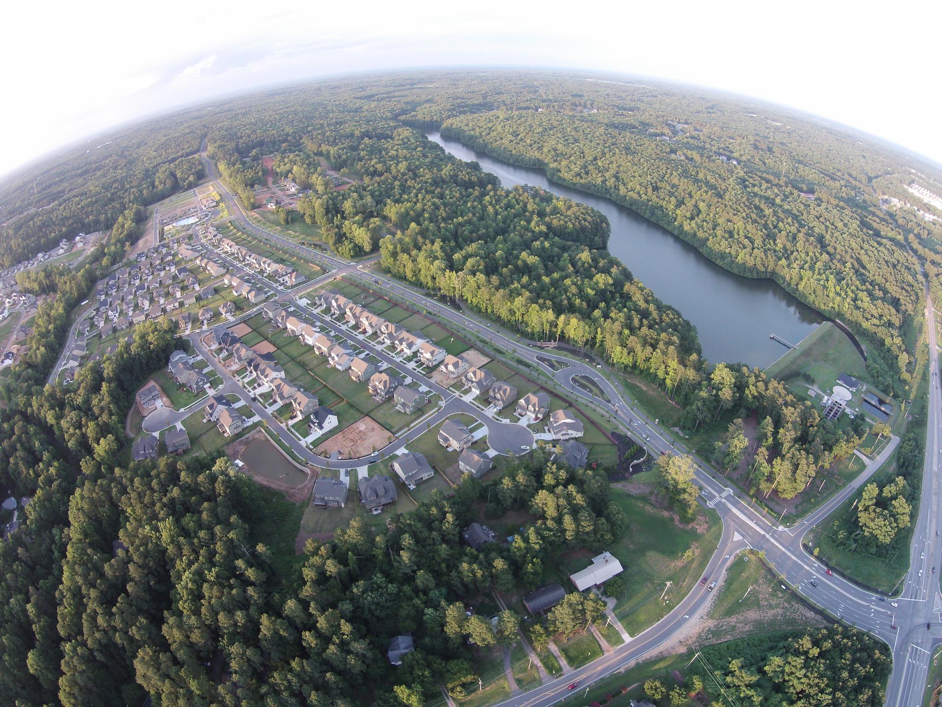 Fisheye aerial view of a residential area, lake, and vast green forest.